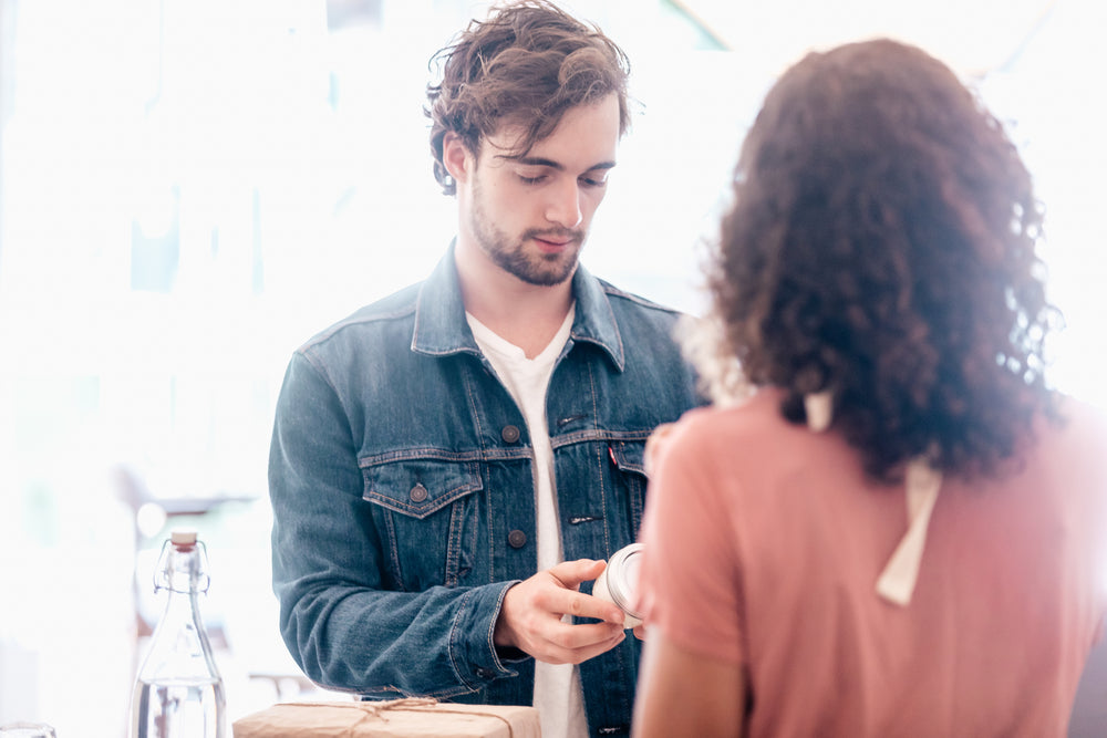 Man in denim jacket receiving a gift from a woman in a casual setting, representing Simply Magnificent’s curated collection of gifts for men.